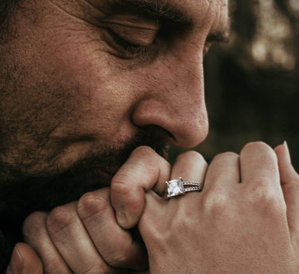 A man kissing his partner's hand, which wears a princess-cut diamond engagement ring
