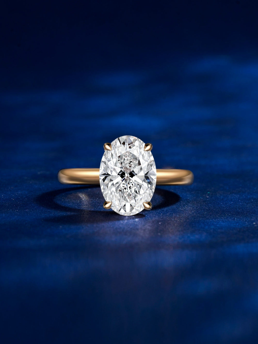 Oval lab-grown diamond solitaire on a gold band, photographed on blue velvet