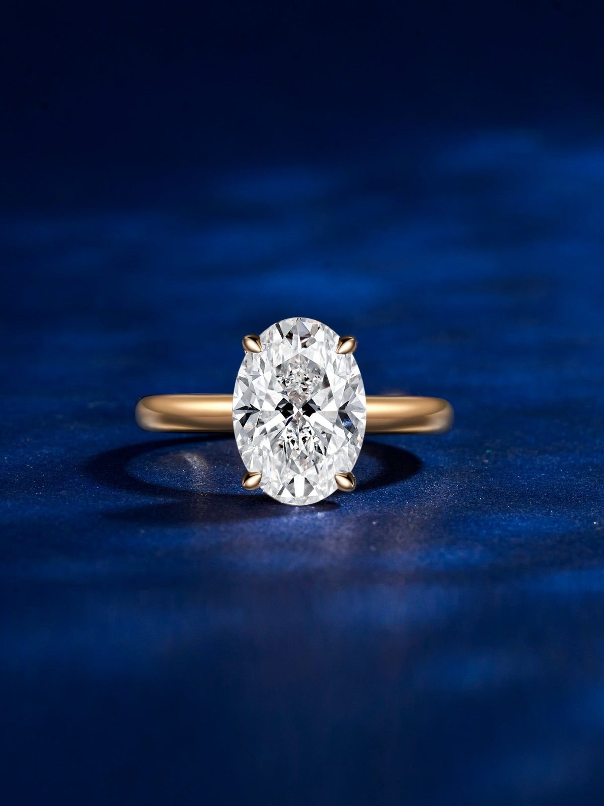 Oval lab-grown diamond solitaire on a gold band, photographed on blue velvet