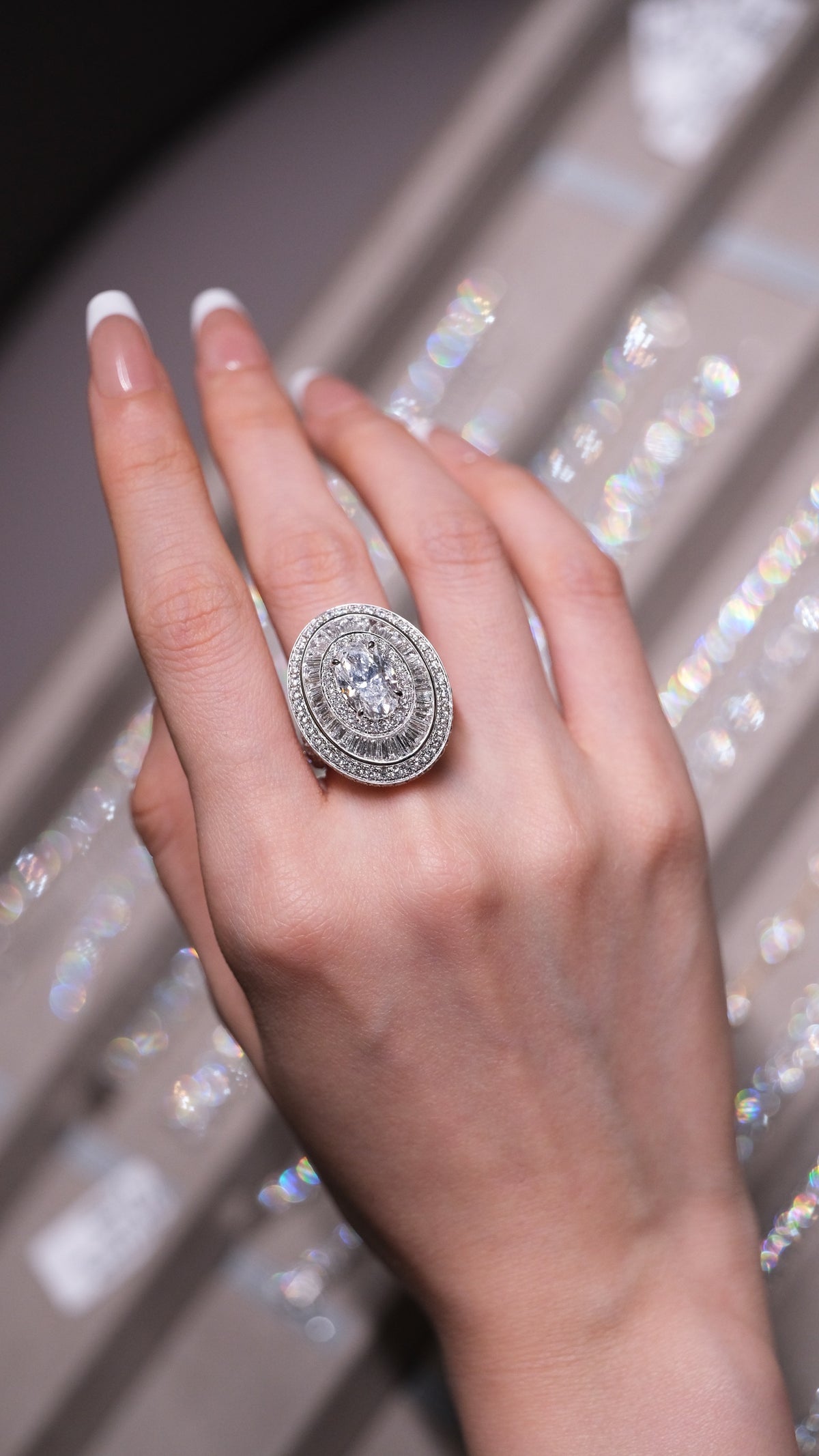 A hand wearing several bespoke diamond rings, resting above a blue bowl with a lily